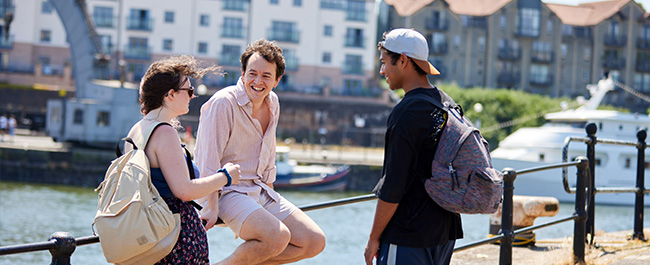 Three students socialise around harbourside.
